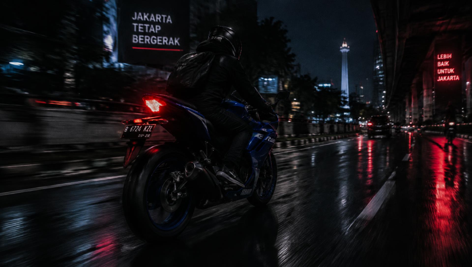 A rider on a sport motorcycle crossing a rain-slick city street at night
